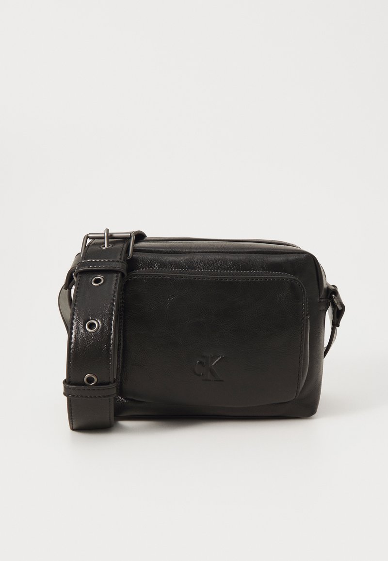 Čierna kožená crossbody taška s textúrovaným povrchom, nastaviteľným popruhom, prednou zipsovou vreckom a embosovaným logom. Kompaktný obdĺžnikový tvar.