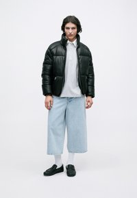 Jachetă puffer neagră, polo gri cu trei butoane, blugi largi de culoare albastru deschis, mocasini negri și șosete albe. Stil simplu, monocromatic.