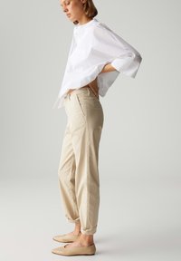 Weißes, locker sitzendes Hemd mit einer Brusttasche; beigefarbene, schmal zulaufende Hose mit aufgerolltem Saum; hellbeige Ballerinas mit spitzem Zeh.