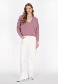 Felpa a V in mauve chiaro con maniche lunghe, design cropped, abbinata a jeans bianchi a gamba larga e sneakers in tela con dettagli rossi.