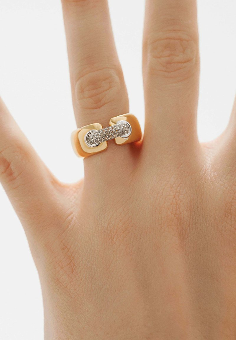Anillo de oro y plata con una banda central de piedras claras, acabado suave y brillante, y extremos en forma de cuadrado.