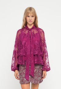 Gjennomsiktig lilla bluse i blonde med knytting i halsen, lagdelt design og lange ermer, kombinert med et strukturert paljettminiskjørt i blandede farger.