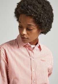Camicia a righe rosse e bianche con colletto, dotata di un sottile logo decorativo e in un morbido tessuto texturizzato.