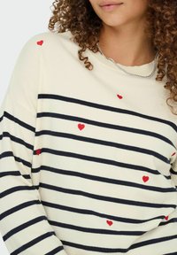 Wit en marineblauw gestreepte sweater met rode hartborduursels, voorzien van een ronde hals en een losse pasvorm, gemaakt van een zachte stof.