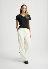Zwart V-hals t-shirt met een subtiele logo op de borst, gecombineerd met losse witte broeken met een elastische taille en zijzakken.