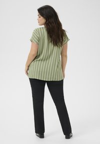 Haut à manches courtes rayé vert avec un ourlet courbé, associé à un pantalon noir à jambes droites et des chaussures noires. Tissu léger, coupe décontractée.