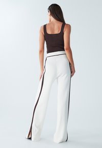Pruun sobiv tank top, mis on kombineeritud valgete soonikkudega laia lõikega pükstega, millel on pruuni värvi külgtriibud ja lõhikud allservas.