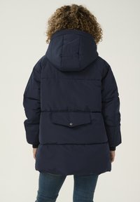Abrigo acolchado azul marino con capucha, que cuenta con un bolsillo trasero con tapa de botón a presión, textura acolchada y puños de canalé.