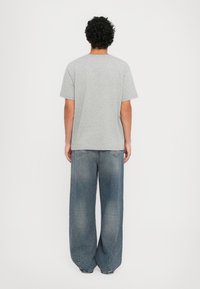 Tricou din bumbac gri, cu mâneci scurte, croială lejeră și guler tip crew, asociat cu blugi de denim albastri cu o croială largă și o textură decolorată.