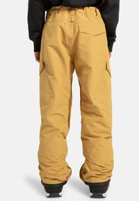 Pantaloni da neve gialli con una vestibilità rilassata, vita elastica e tasche cargo. Realizzati in materiale impermeabile con una consistenza liscia e cuciture resistenti.