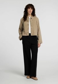 Beige denimjacka med metallknappar, avslappnad passform, bärs över en vit topp, matchad med svarta vida byxor och nakna ballerinas.