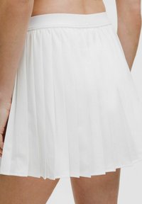 Jupe plissée blanche en tissu léger. Dispose d'une taille plate avec un logo discret à l'arrière et une texture lisse.