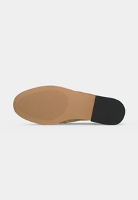 Semelle d'une chaussure habillée avec l'avant lisse couleur fauve et une partie talon texturée noire, présentée sur un fond clair uni.