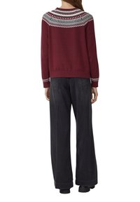 Bordowy sweter z dzianiny z okrągłym dekoltem, zdobiony misternym wzorem w odcieniach szarości i bieli na ramionach i mankietach. Połączony z szerokimi, szarymi spodniami.
