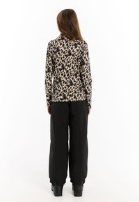 Dlhý rukáv top v krémovej a čiernej zvieracej potlači, skombinovaný s voľnými čiernymi nohavicami. Nohavice majú nastaviteľné manžety a čierne topánky.