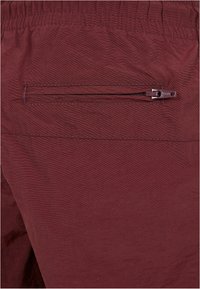 Pantaloni corti color bordeaux in un tessuto leggero e testurizzato. Presentano una tasca posteriore con zip e una vita elastica.