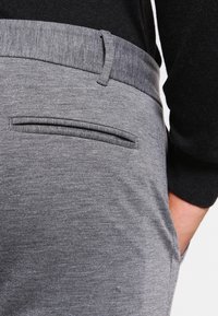 Grå byxor med en slät textur, med en smal passform, en sidoficka och ett åtsittande midjeband. Tyget har ett subtilt melerat mönster.