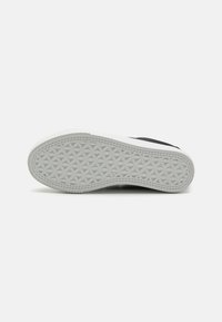 Black sneaker sole with a white rubber bottom featuring a geometric pattern. Reinforced edges and textured grip surface.
