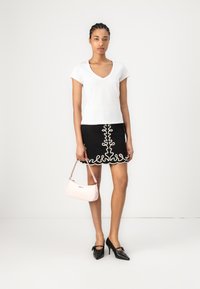 T-shirt blanc à col en V, jupe noire avec broderie en dentelle blanche, sac à main rose et escarpins noirs avec accent en nœud.
