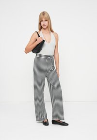 Bodysuit cinza sem mangas combinado com calças largas às riscas pretas e brancas. A modelo segura uma mala preta e usa sapatos planos pretos.