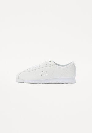 Biały niski sneaker z sznurowaniem, gładką skórzaną cholewką, subtelnymi perforacjami oraz srebrnym logo krokodyla po boku.