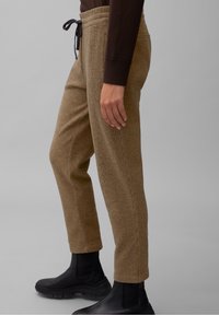 Bruine tweed joggers met een gestructureerde stof, taps toelopende pasvorm, elastische tailleband en trekkoord, gecombineerd met zwarte enkellaarsjes.