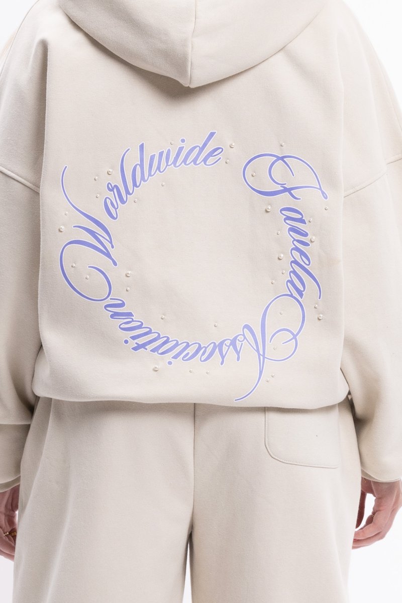 Béžová oversized mikina s veľkým fialovým textovým dizajnom na chrbte, doplnená malými bielymi perlami. Mäkká tkanina a uvoľnený strih.
