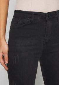 Jeans de denim negros con un ajuste slim, sutiles detalles desgastados, bolsillos frontales y una cintura clásica con un cierre de botón.