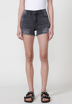 Schwarze Jeansshorts mit einer ausgewaschenen Optik, fransigem Saum und zwei vorderen Taschen, kombiniert mit schwarzen Sandalen mit dekorativen Riemen und Schnallen.