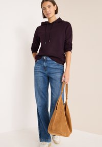 Sudadera morada oscura con cordón, jeans azul claro y un bolso de ante color beige. Zapatillas con acentos en blanco y beige.