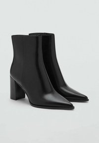 Botas de cuero negras hasta el tobillo con punta afilada y tacón cuadrado. Textura suave y diseño minimalista. Cierre de cremallera en la parte trasera.