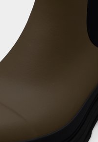 Καφέ λαστιχένια μπότα με λείο υφή, με μαύρη λεπτομέρεια γύρω από τον αστράγαλο και παχύ, υφή πέλμα για καλύτερη πρόσφυση.