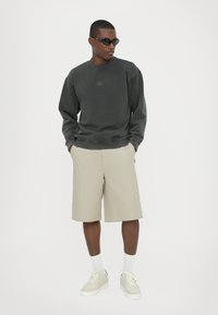 Grå sweatshirt med et lille logo, beige shorts, hvide sokker og lyse sneakers. Glat stof, afslappet pasform, minimalistisk design.