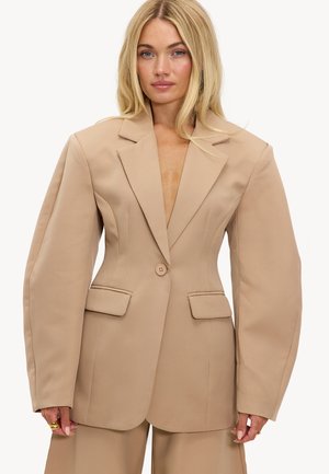 Beige oversized blazer met gestructureerde schouders, enkele knoopsluiting, twee frontzakken, gemaakt van gladde stof. Opvallend diep V-hals ontwerp.