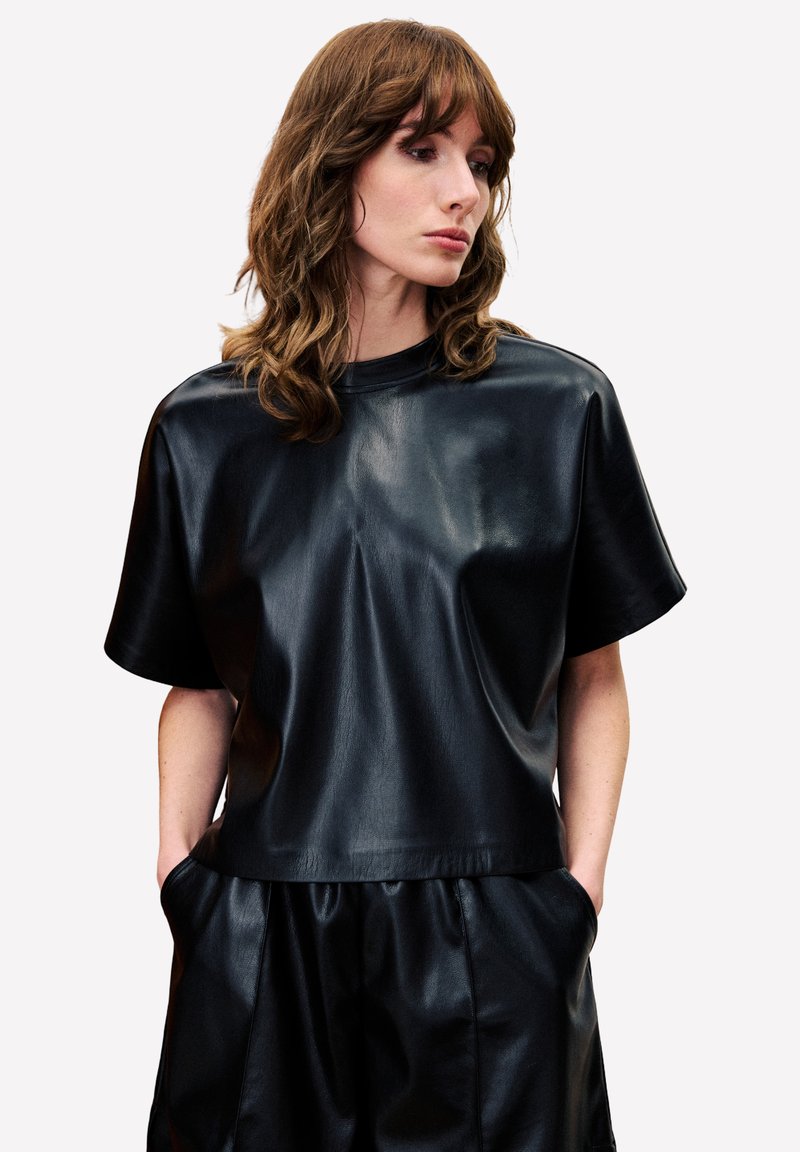 Zwarte faux leren top met korte mouwen, in een relaxte pasvorm en met een ronde halslijn, voorzien van een gladde textuur en een minimalistisch ontwerp.