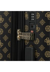 Valigia nera con motivo a logo dorato, doppi zip dorati contrassegnati "GUESS" e una combinazione approvata dalla TSA sul lato.