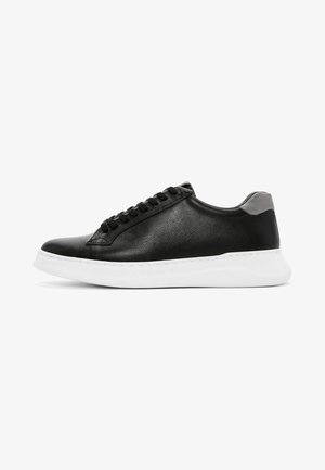 Zwarte leren sneaker met een textuurafwerking, voorzien van een witte rubberen zool, grijze hakaccent en zwart vetersysteem.