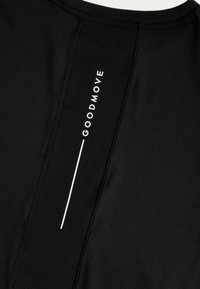Camiseta deportiva negra con panel texturizado, logo blanco "GOODMOVE" y un detalle de línea blanca vertical en la parte posterior.