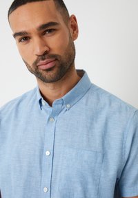 Camicia button-up azzurro chiaro con colletto, dotata di taschino sul petto, tessuto testurizzato e leggera variazione di colore.