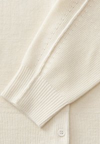 Gebreide cardigan in crème, met een gestructureerd patroon, ribbels aan de mouwen en een witte knoop. Zachte stof met een gezellige uitstraling en gedetailleerde stiksels.