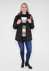 Doudoune noire rembourrée avec une fermeture éclair et des poches latérales. Portée par-dessus un pull rayé, associée à un jean bleu et des bottines noires.