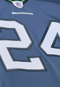 Graues Sporttrikot mit der weißen Nummer "26" und dem Text "Seahawks". Es hat einen strukturierten Stoff und kontrastierende Nähte entlang der Zahlen.