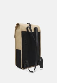 Canvasryggsäck i beige och svart, med justerbara svarta remmar, rulltoppsstängning och en sidoficka med dragkedja för extra förvaring.