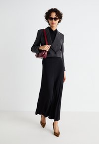 Grauer Streifenanzug mit doppelter Knopfleiste, schwarzes Oberteil, schwarze fließende Rock, High Heels im Leopardenmuster, bordeauxfarbene Umhängetasche, Sonnenbrille.
