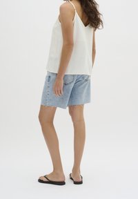 White satin camisole with thin straps, paired with light blue distressed denim shorts that have frayed hems and pockets. Black flip-flops.