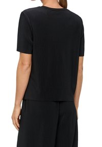 Top corto negro de canalé con cuello redondo, que presenta un ajuste holgado y una textura suave, combinado con pantalones a juego de canalé.