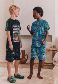 Sort T-shirt med grøn Minecraft-tekst, sorte shorts med mønster og grønne slip-on sko; blå mønstret skjorte og shorts med Minecraft-designs.