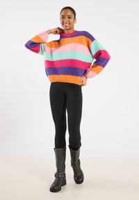 Colorful oversized sweater featuring horizontal stripes in shades of pink, orange, teal, and purple; paired with black leggings and knee-high boots.