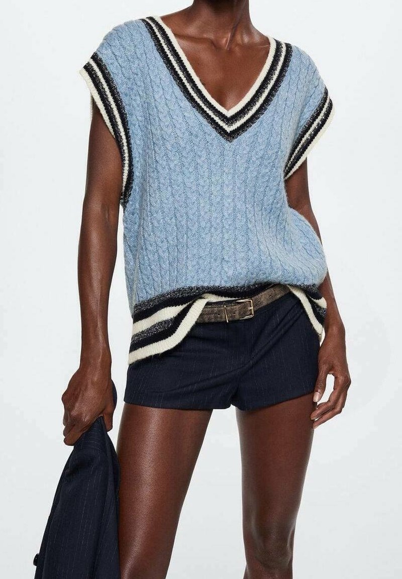 Personne portant un pull sans manches en maille torsadée bleu clair avec des bordures rayées blanches et noires, un short marine, et tenant une veste marine.