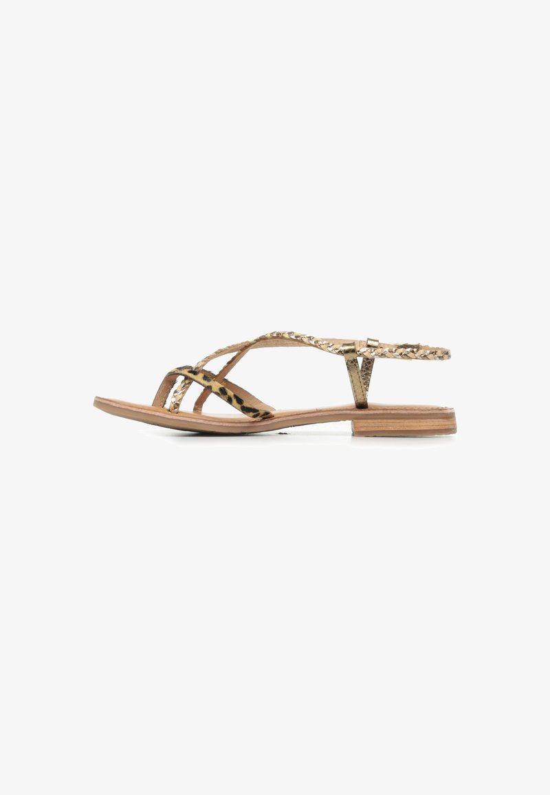 Sandali flat a motivo oro e nero con cinturini incrociati, caratterizzati da un design intrecciato e una suola sottile e piatta di tonalità legno naturale.
